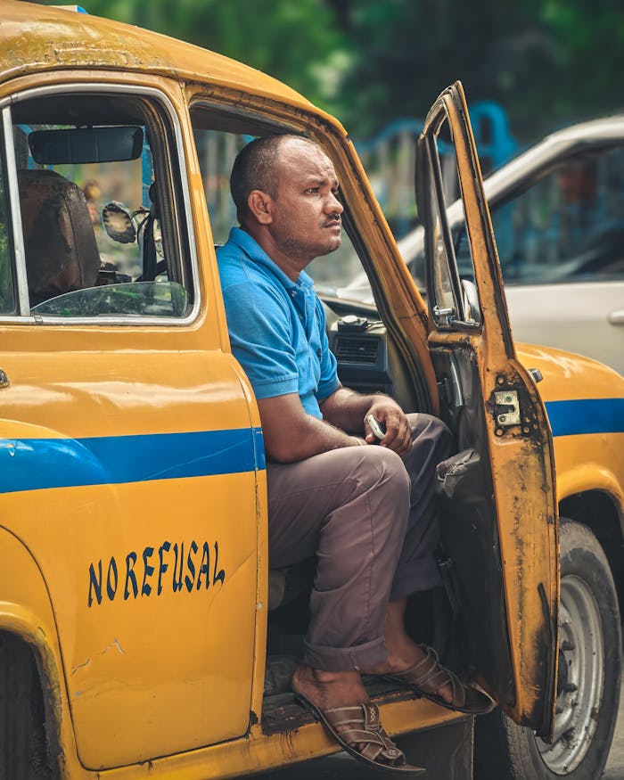 A man sits in an iconic yellow taxi in Kolkata, India, conveying local transportation essence.