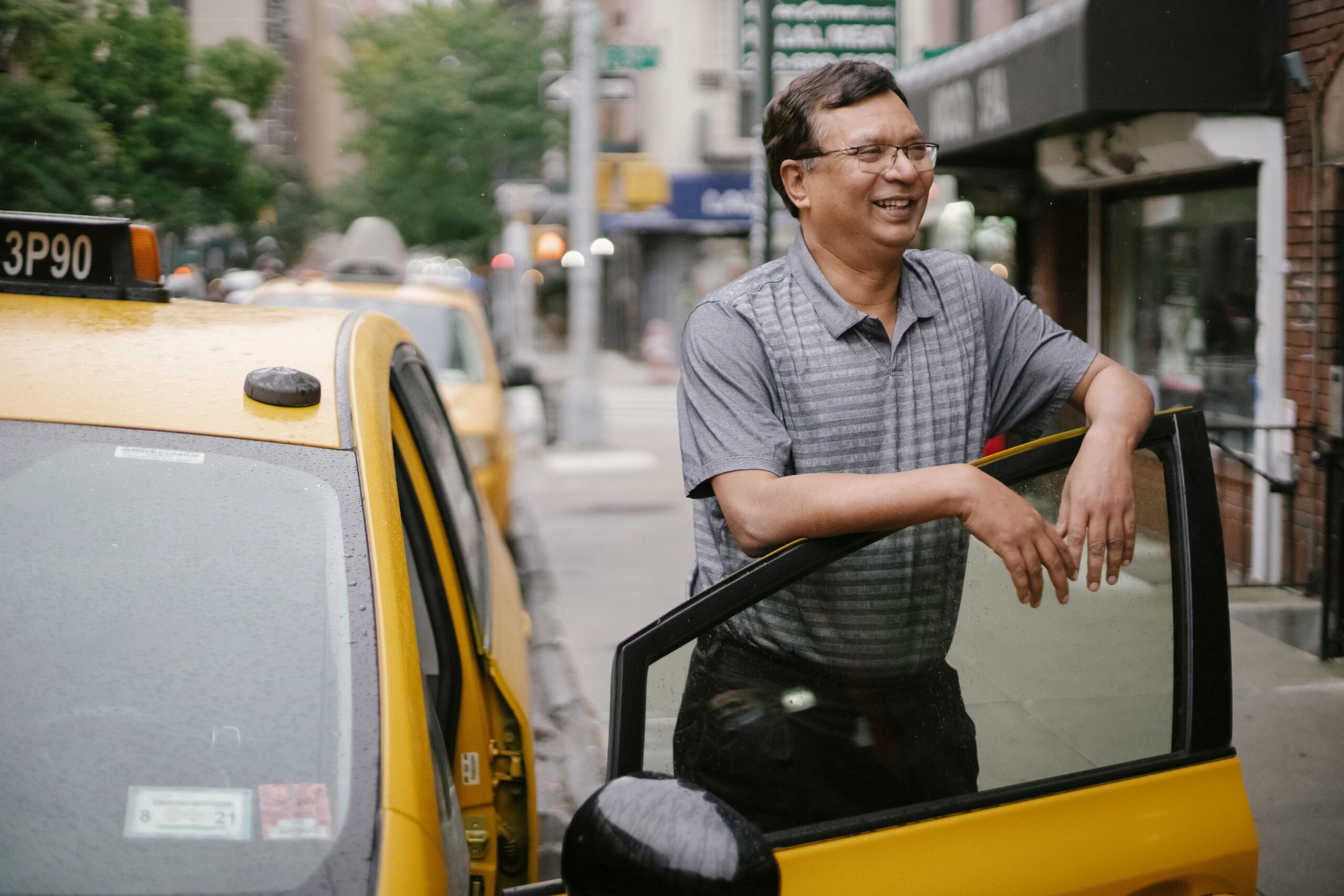 Happy man with glasses smiling and standing near yellow taxi on street in city in daytime