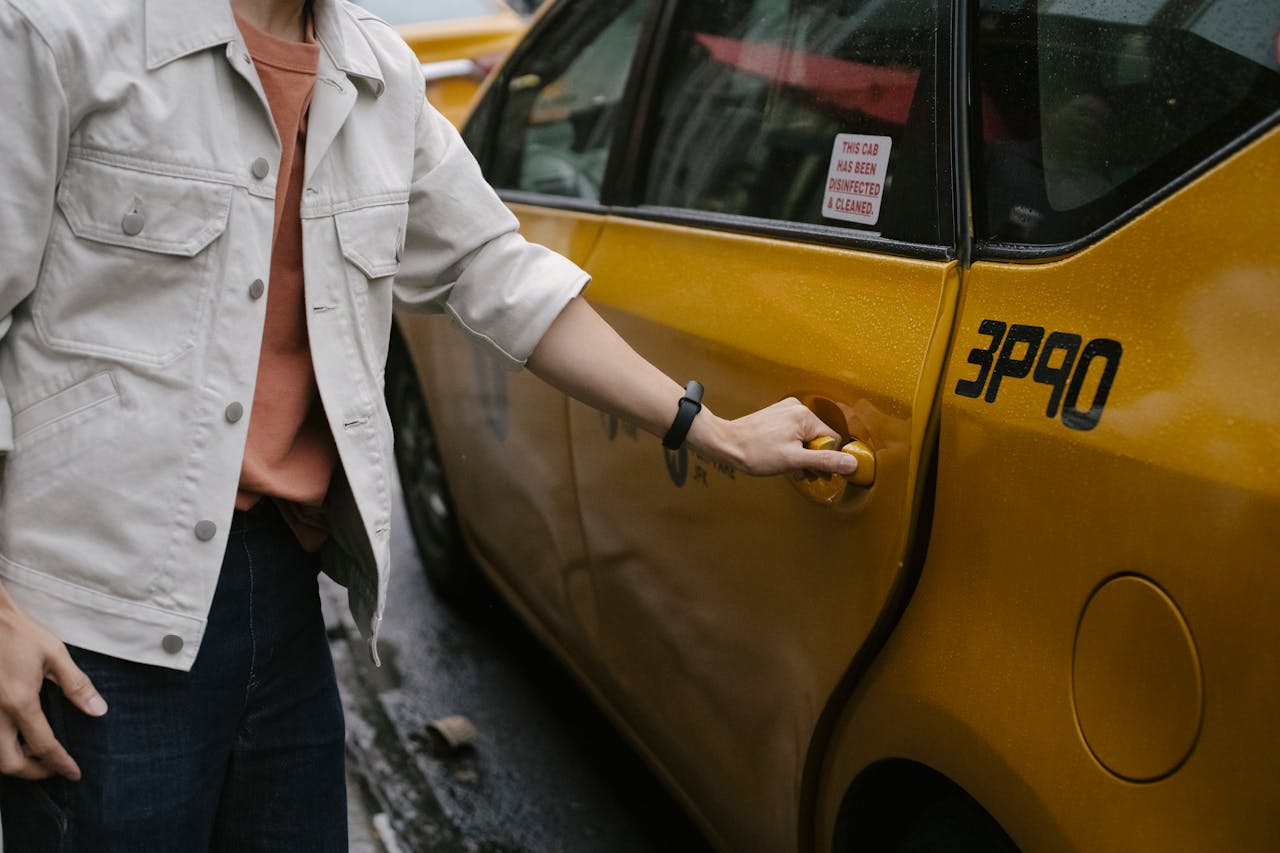 Unrecognizable passenger in casual clothes opening door of cab parked on roadside in city on street while commuting to work
