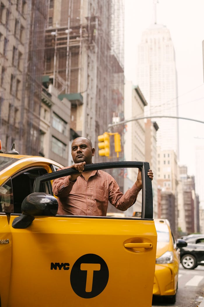 Low angle of ethnic male driver in casual clothes going out of taxi while having break during work in city