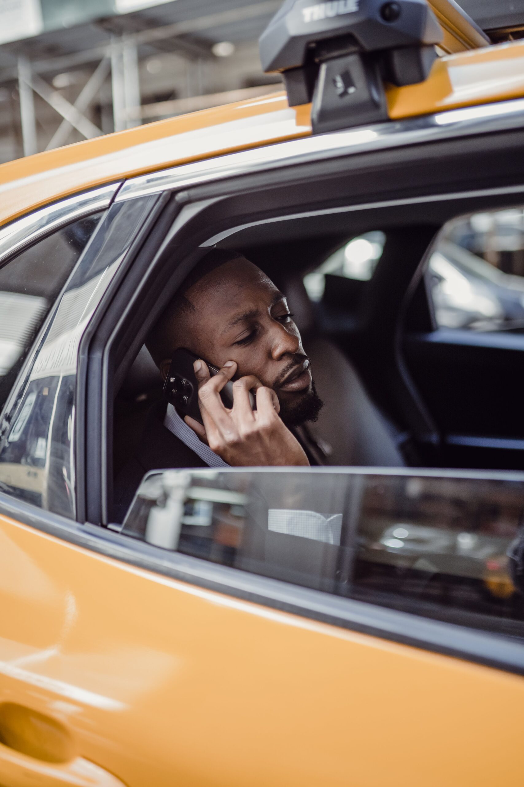 African American man talking on phone inside a yellow taxi cab, urban setting.